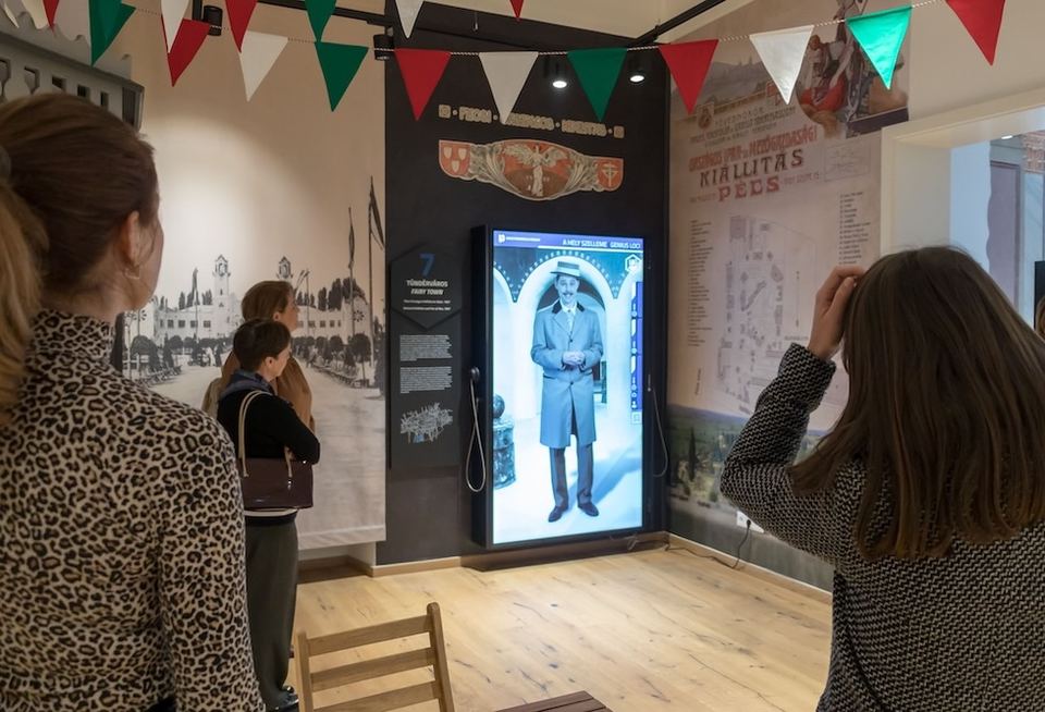Life-size digital e-poster of the Genius Loci exhibition with visitors at the Janus Pannonius Museum, Pécs